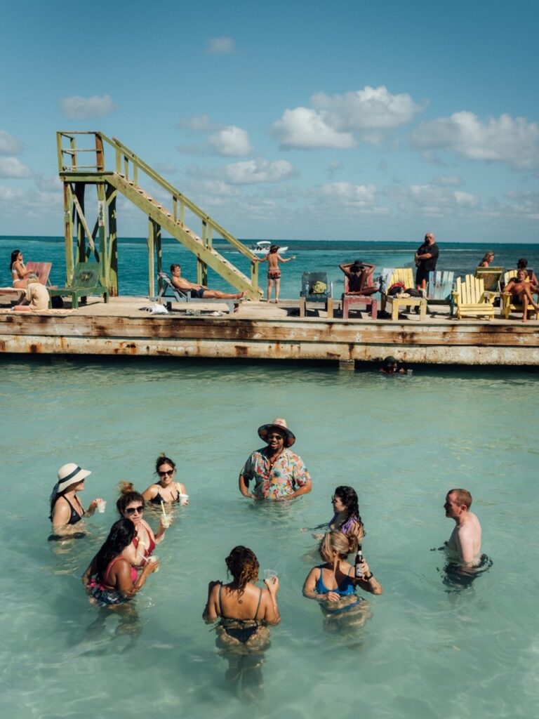 A bunch of people wade in the water by a wood deck.