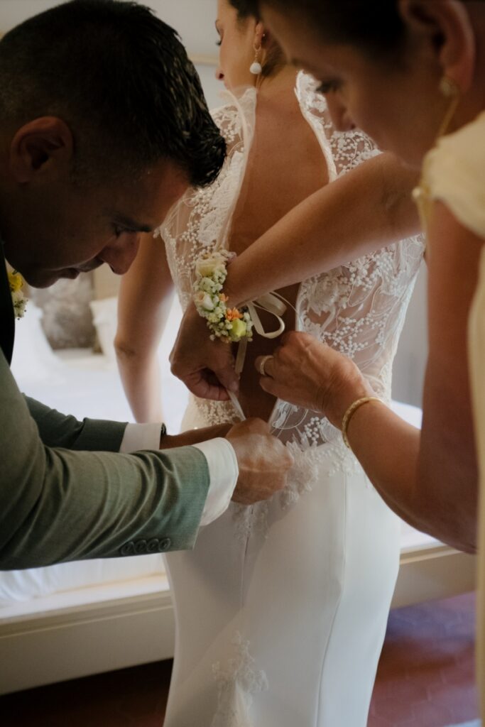 A close-up of a bride in a lace Ines de Santo wedding gown being helped into her dress by family members before her wedding.