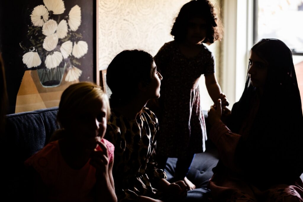 A candid silhouette of Fatima and Shelley’s children interacting and holding hands in a sunlit living room during a cross-cultural family gathering.
