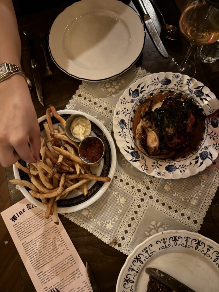 A person reaches for a plate of french fries sits beside another plate of meat.
