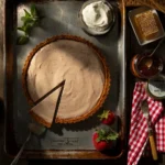 HoneyRum Strawberry Jam Semifreddo Tart in a graham cracker crust with a single slice removed, surrounded by fresh strawberries, whipped cream, and honeycomb.