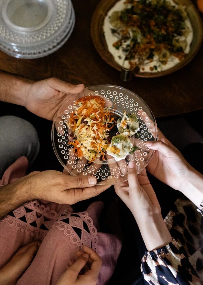 Immigrant Resources Strengthening Pittsburgh Communities Two hands reach for a plate of immigrant cultural cuisine ina. slaw and dumplings.