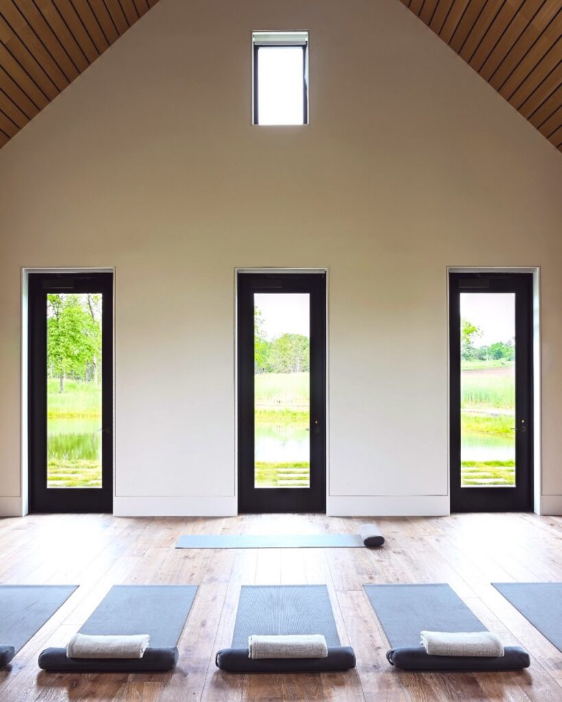 A yoga room with a high ceiling and bright windows with mats on the floor.