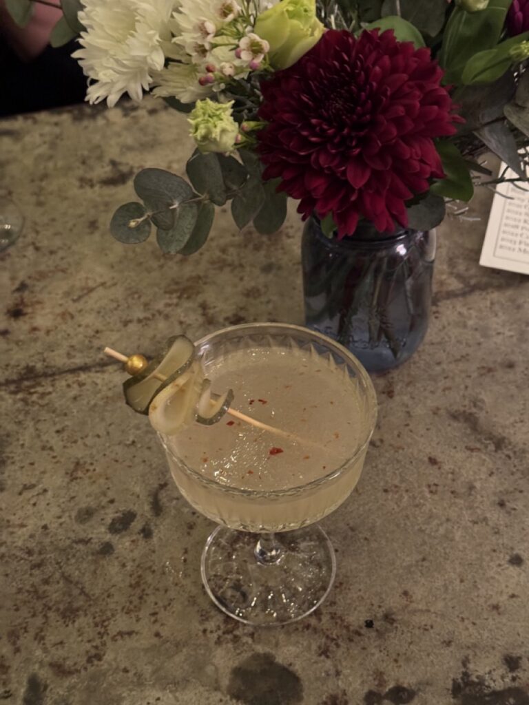 A cocktail sits on a table with red flowers.
