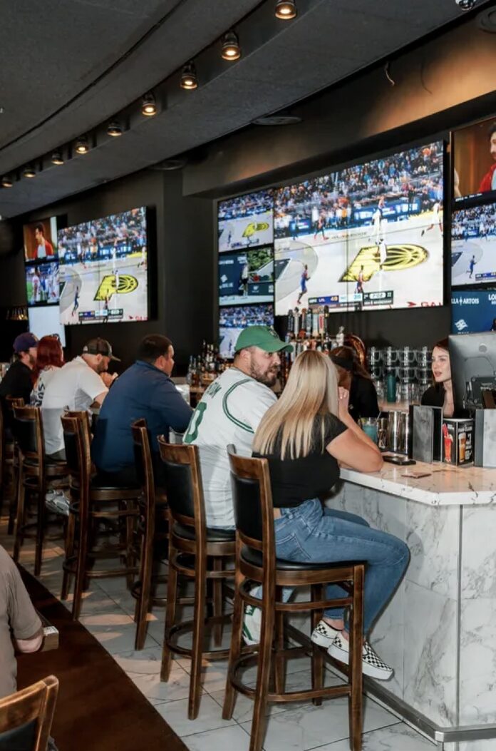 People sit at a bar watching a basketball March madness game on a TV.