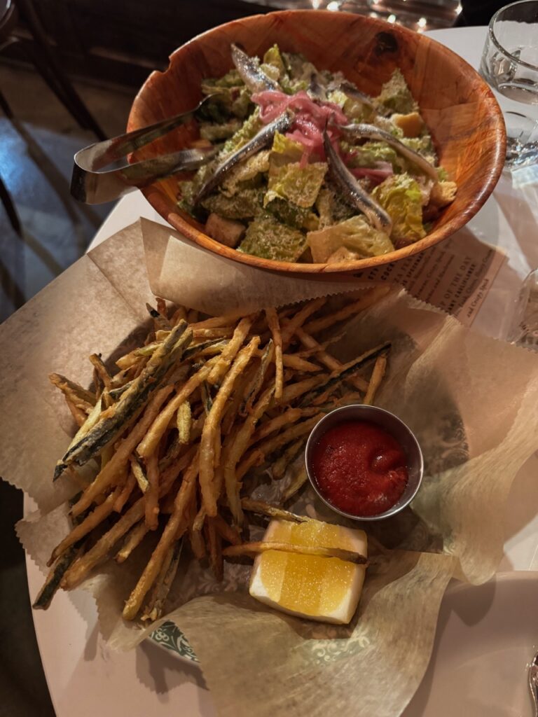 A basket of fries sits below a bowl of a caesar salad.