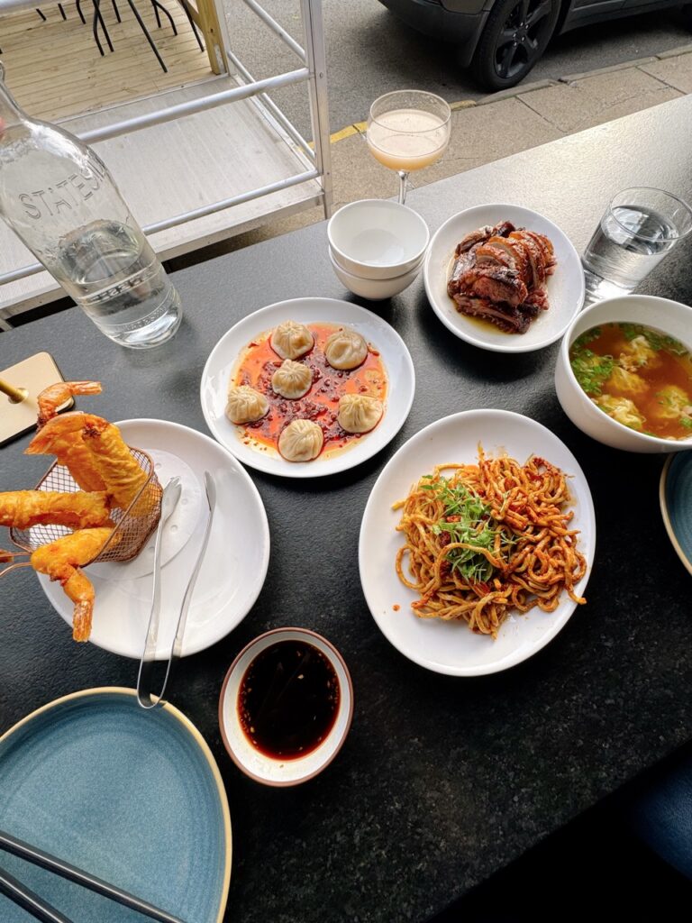 A black table with Asian-style dishes all over it like dumplings, noodles, and prawns.