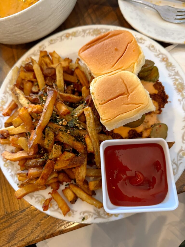 A white plate full of french fries and two sliders with a side of red sauce.