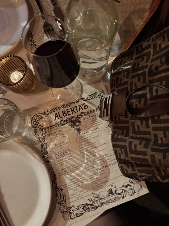 A menu for Alberta's lays on a table by a purse and wine glasses.