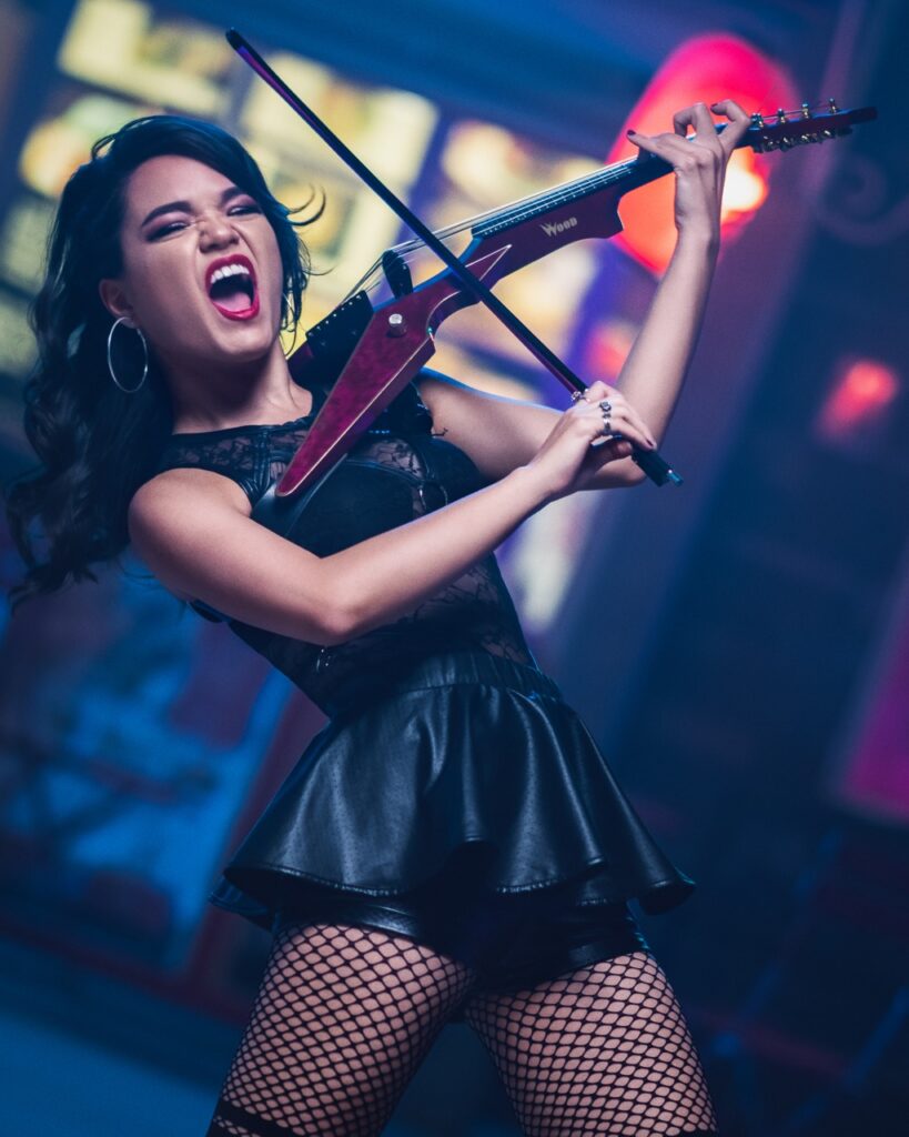 Mia in a black dress on stage playing her violin.