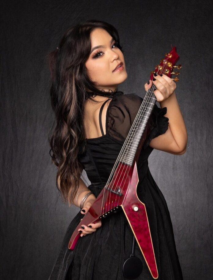 Mia Asano in a black dress with her red flying v violin over her shoulder.