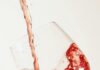 4 Must-Try Bottles of Wine in 2026 Red wine pours into a wine glass against a wine background.