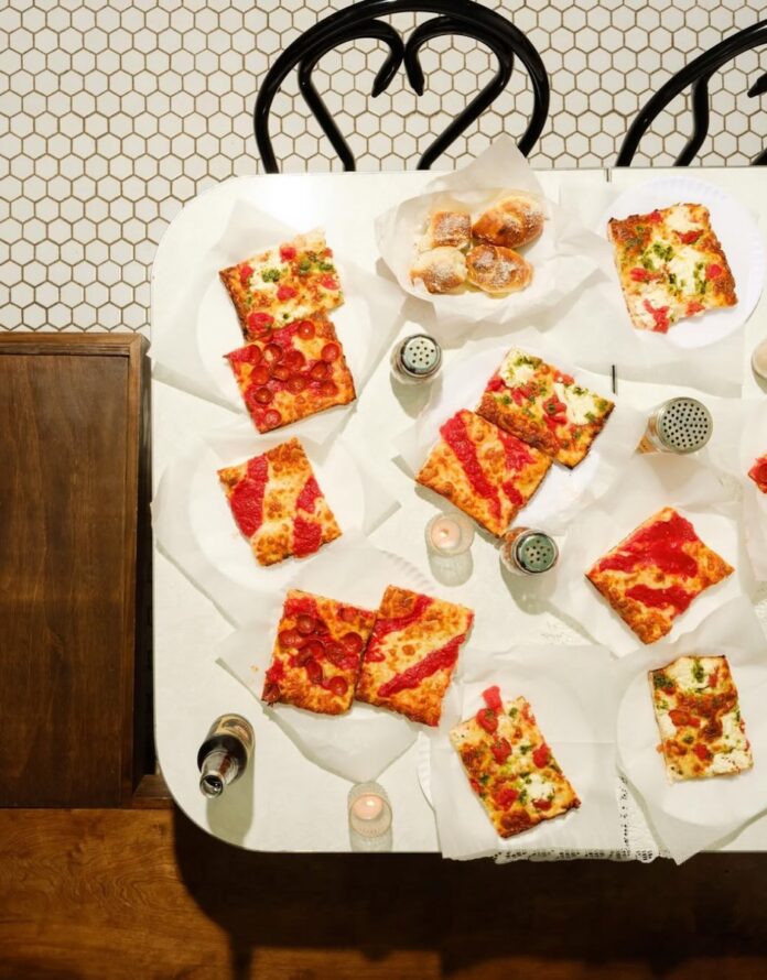 A white table has plates of square pizza all over it.