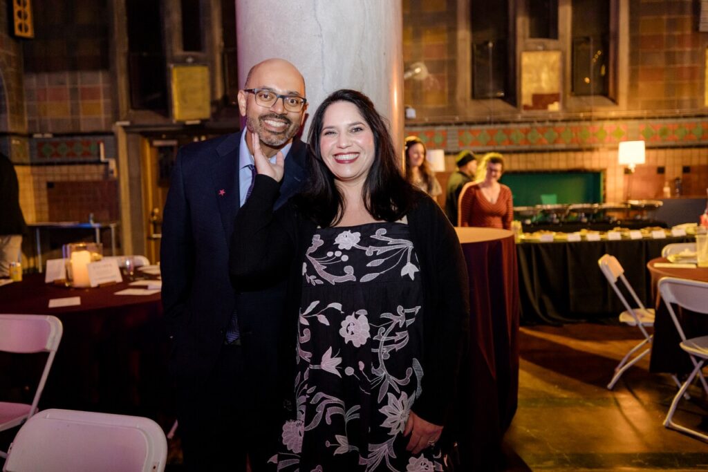 A man in a blue suit and a woman in a black dress smile together.