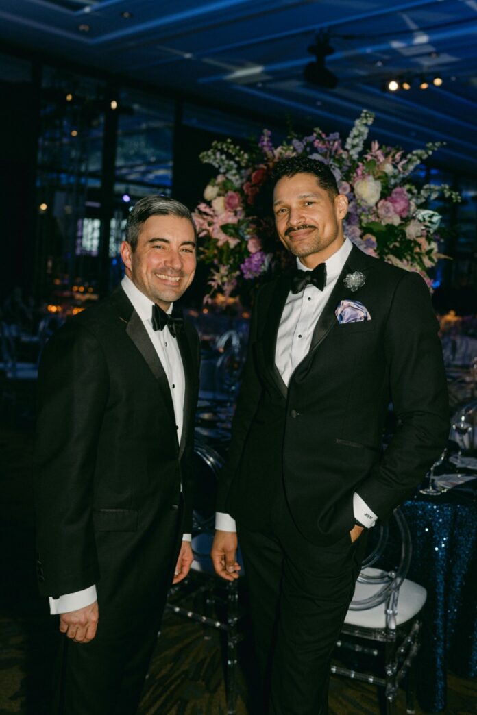 Two men in tuxes stand together.