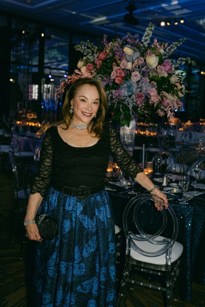 A woman in a black and blue dress stands next to a chair.