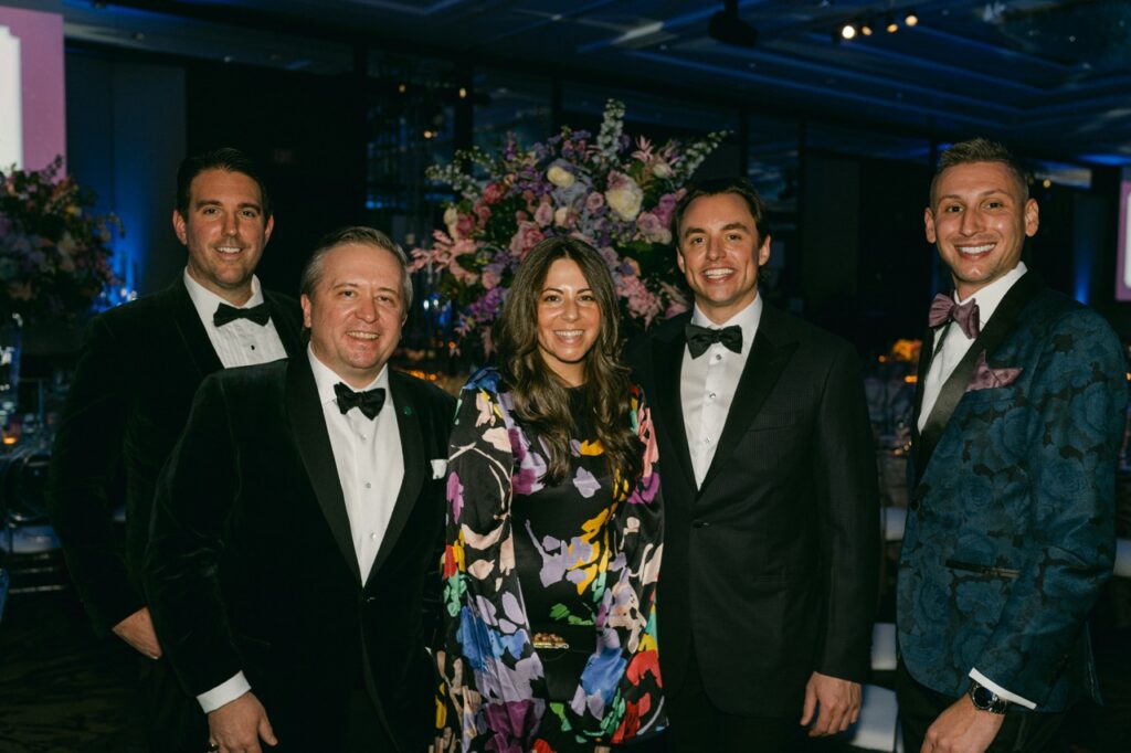 Three men in black tuxes and one in a pattern tux with a woman in a colorful floral dress.