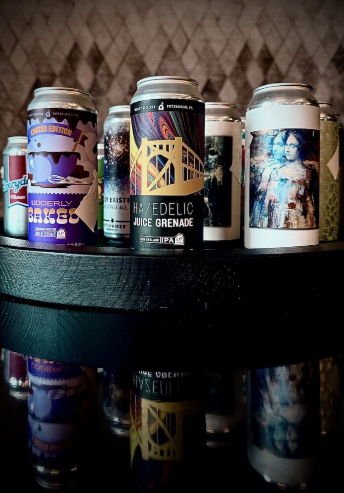 Tall beer cans stand on a tray, reflected in the table below them.