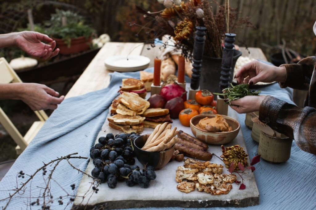 A rustic autumn charcuterie board on a marble slab, featuring grilled cheese sandwiches, dark grapes, roasted cauliflower, and sausages.