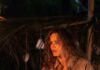 On the Beach, for Better and for Worse: ‘Send Help’ Movie Review A woman stands holding a large stick in the firelight.