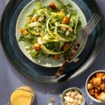 A plate full of shaved asparagus and croutons with a salad dressing container in the bottom left corner.