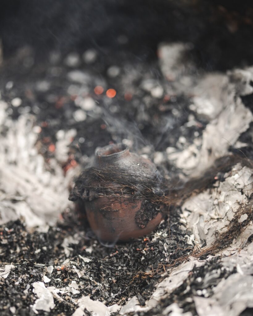 A smoke-stained ceramic pot sitting among ashes and burnt foil after being fired with horsehair in a primitive outdoor kiln.