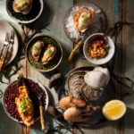 A rustic seafood platter featuring steamed prawns, mussels, and clams topped with Spicy Giardiniera Pimento Cheese, served on beds of colorful legumes and garnished with fresh herbs and lemon.