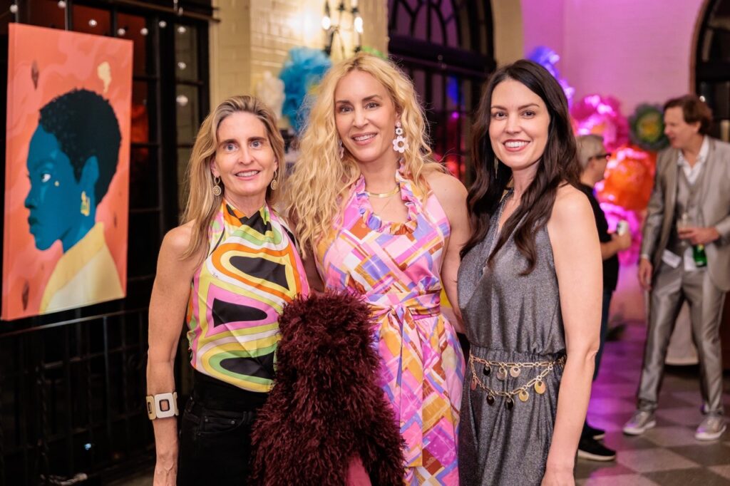 Three women in dresses stand together a a bling ding party.