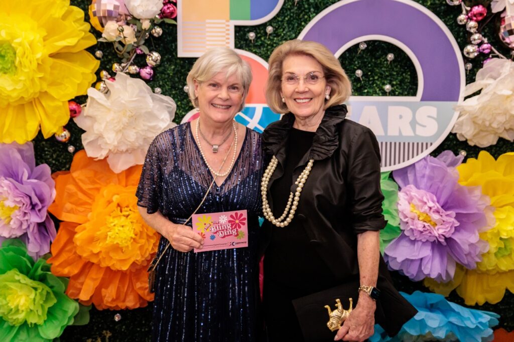 A woman in a blue dress and a woman in a black dress stand together for the bling ding.