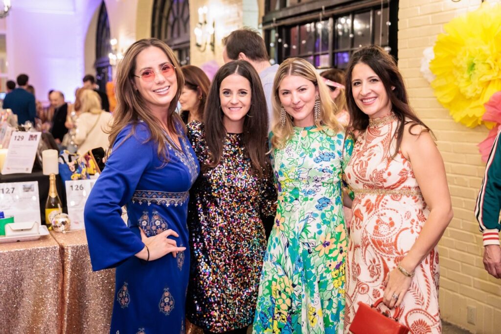 Four women in colorful dresses stand together.