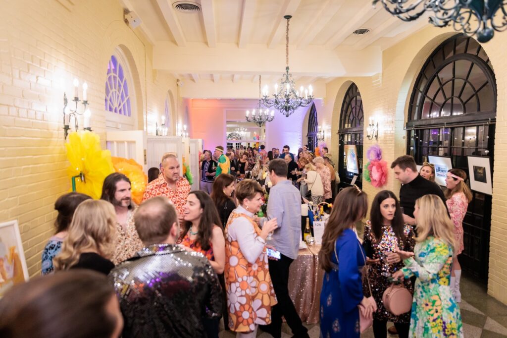 A crowd of people gather in a white brick party room.