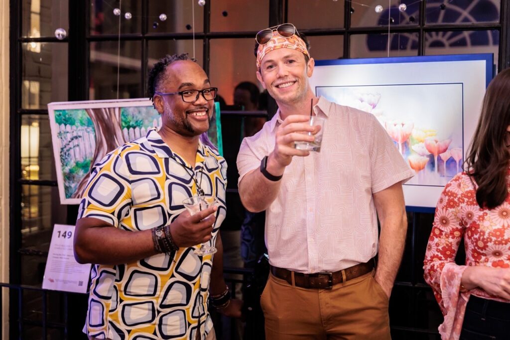A man in a pink shirt stands with a man in a pattern shirt.
