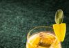 Teacher’s Pet (Laird’s Apple Brandy Cocktail) A bright yellow Teacher's Pet cocktail with apple brandy and sage honey, garnished with a lemon peel and sage leaf in a unique glass.