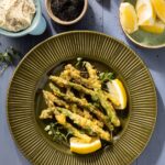 A green plate of lightly fried asparagus tempura with slices of lemon around it.