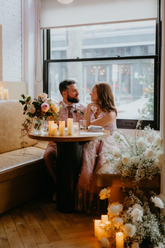 A couple sitting in a private booth at The Vandal in Pittsburgh, sharing a romantic candlelit dinner during their wedding renewal celebration.