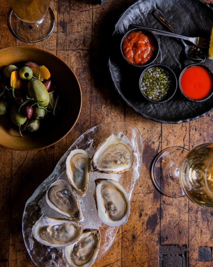A platter of oysters sits on a plate with a plate of olives above it.