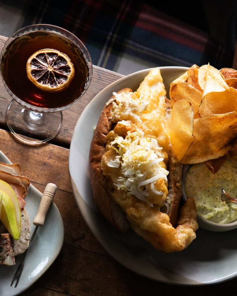 A plate of a fish sandwich and chips beside a cocktail.