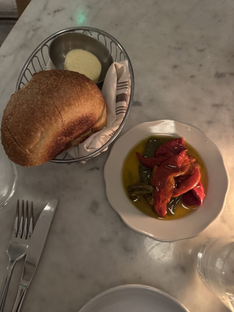 A basket of bread and a plate of peppers sit on a white table.