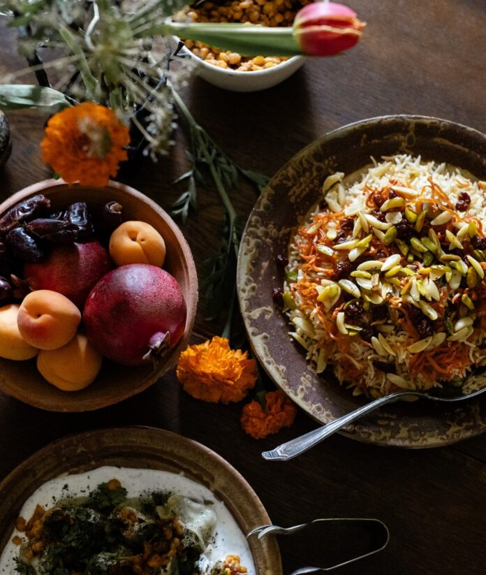 Traditional Afghan Kabuli Pulao with lamb, raisins, and carrots, served alongside fresh apricots, pomegranates, and dates at a community feast.