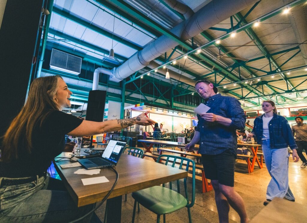 A man turns in his trivia sheet to a woman at a table.