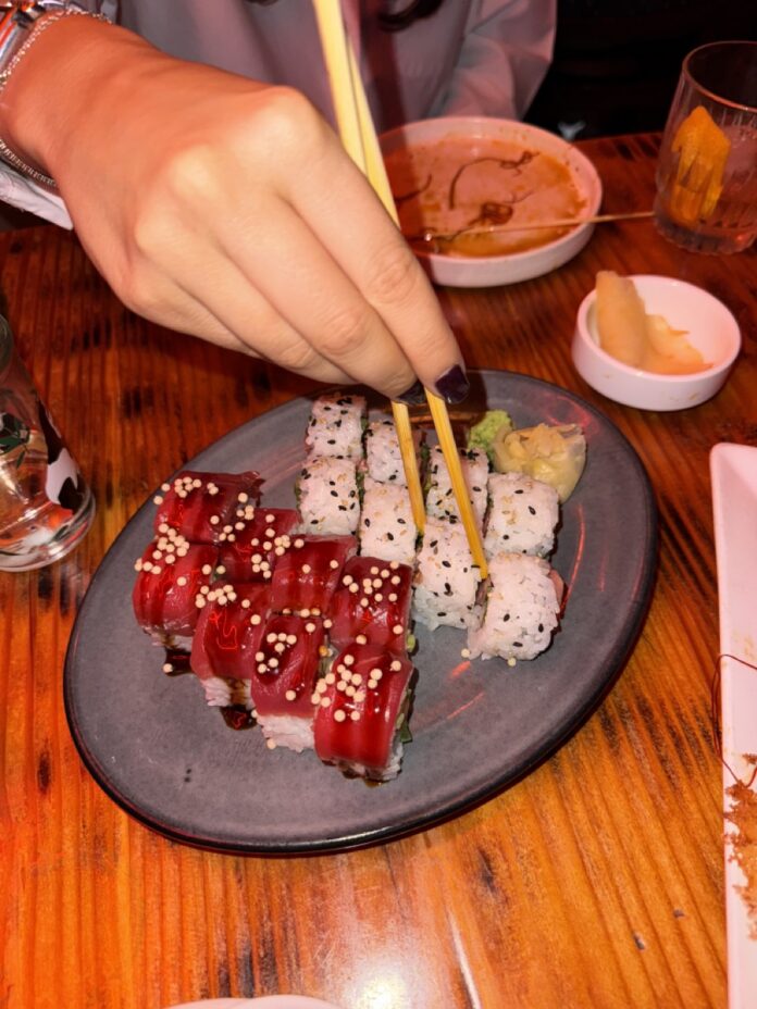 A person uses chopsticks to grab a piece of sushi on a plate.