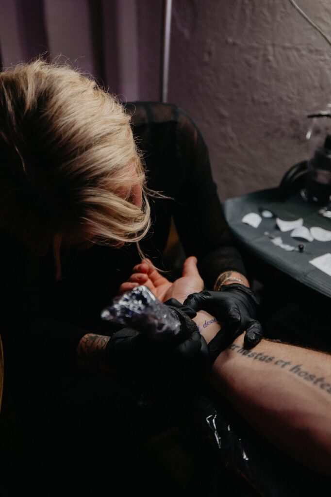 A woman tattoos a persons arm.