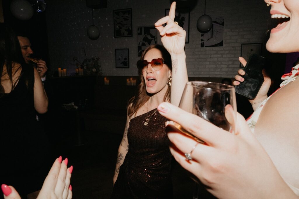 A woman dance and sings with her hand up and sunglasses on.