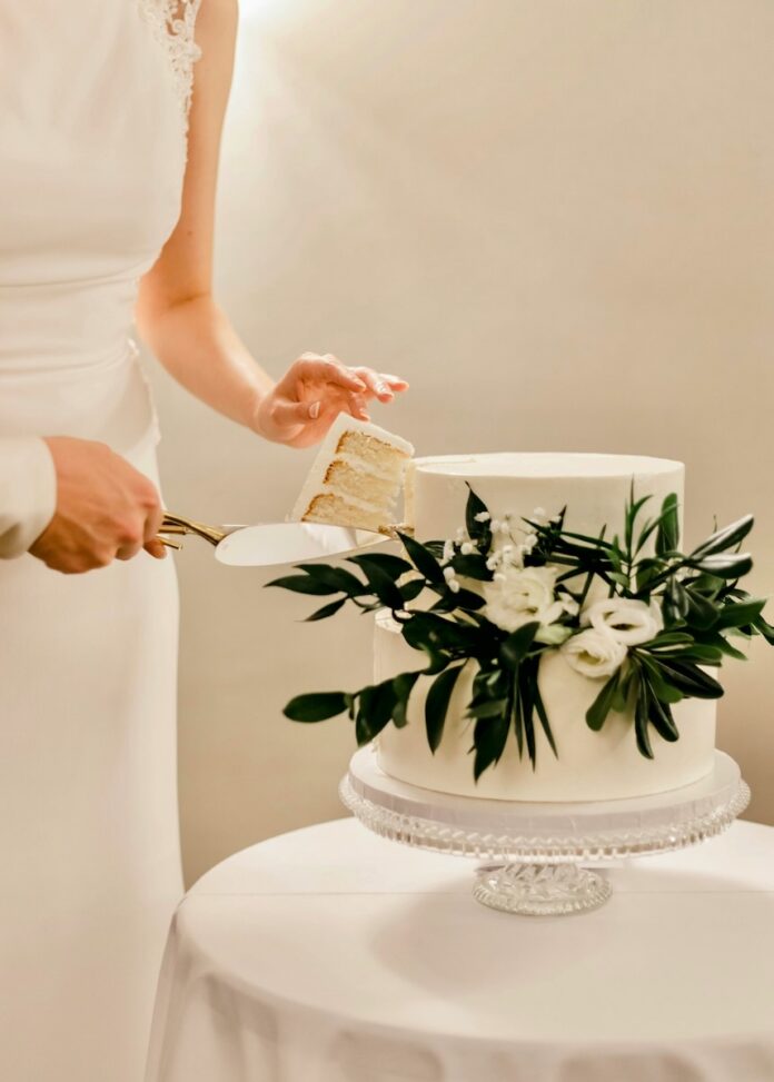 A bridge cuts a slice of wedding cake with florals embellishing it.