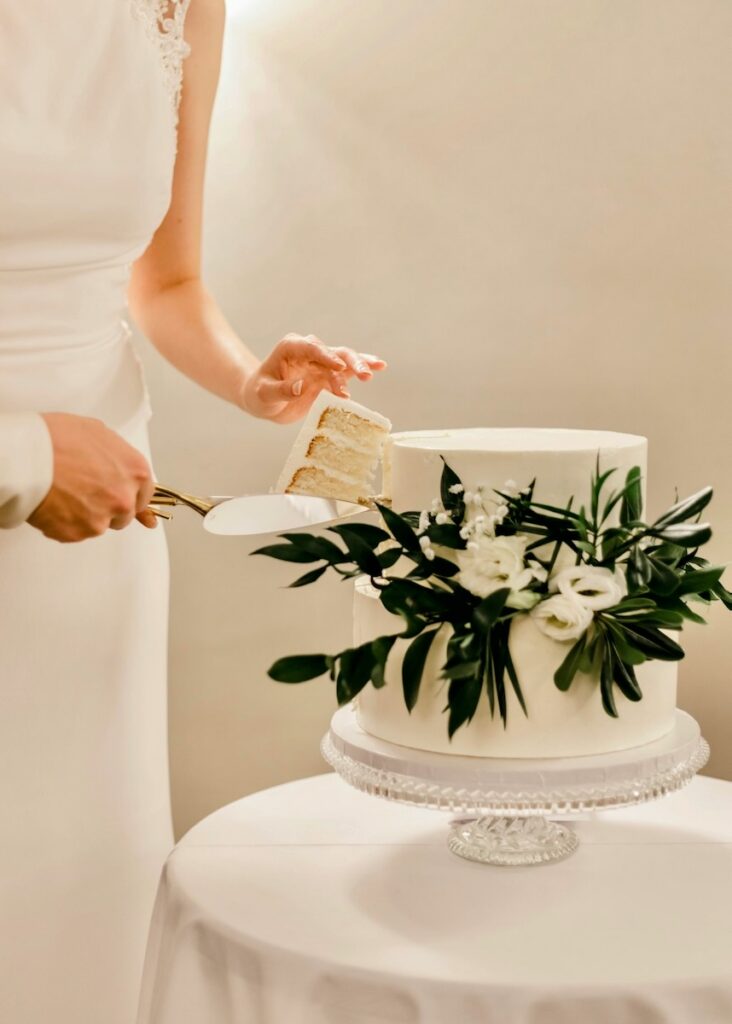 A bridge cuts a slice of wedding cake with florals embellishing it.