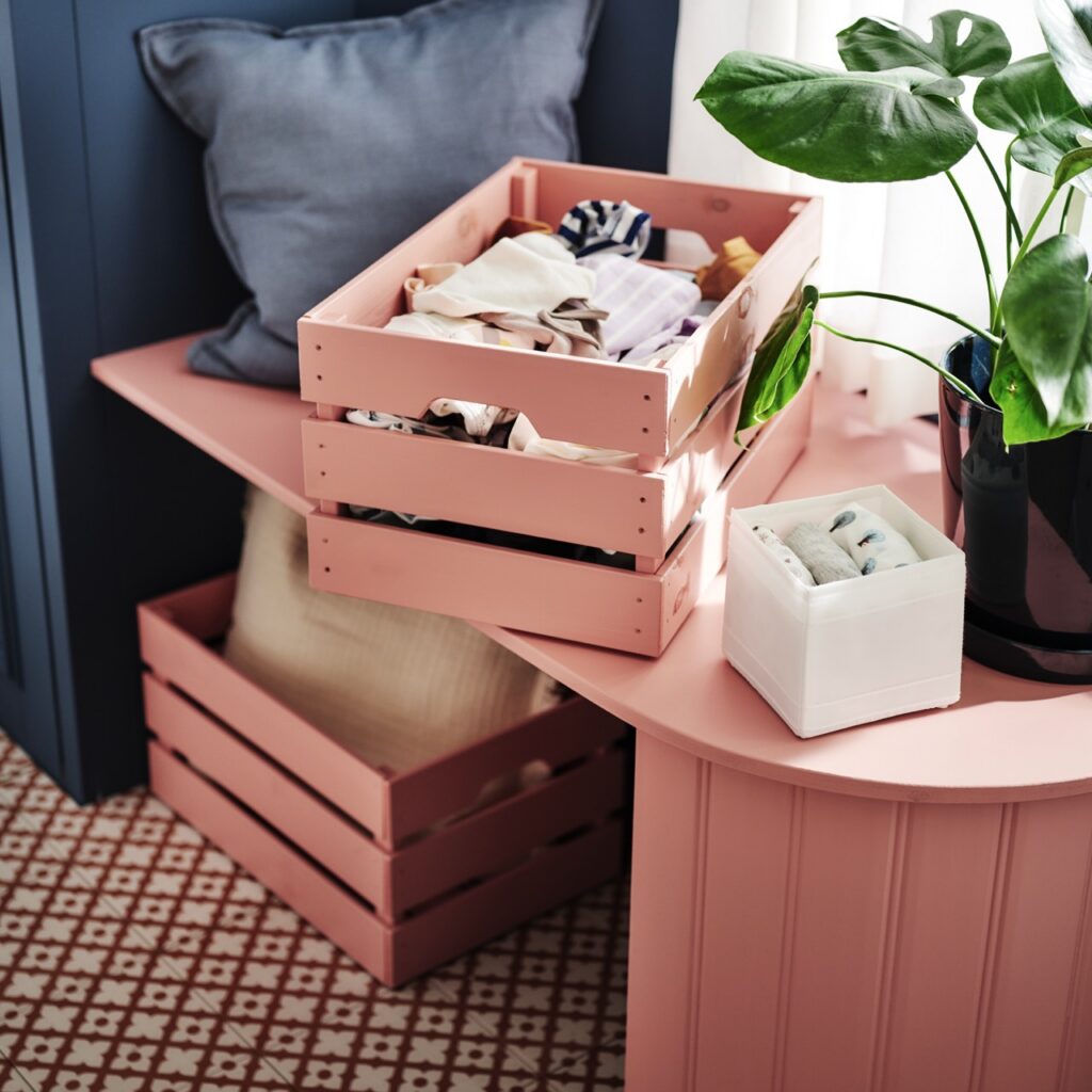 Pink crates sit on top of a pink table along with a potted plant.
