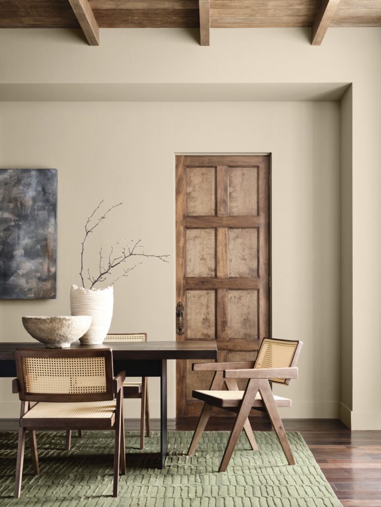 A wood door is against a beige wall with a table and chairs in the center of the room.
