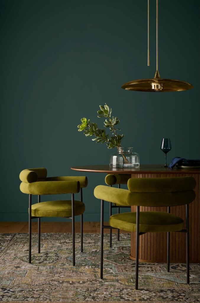 Green dining chairs and a table set sit against a dark teal wall.