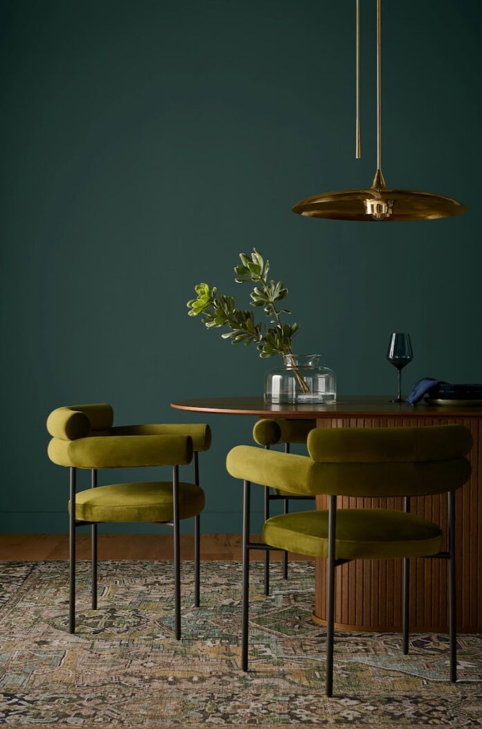 Green dining chairs and a table set sit against a dark teal wall.