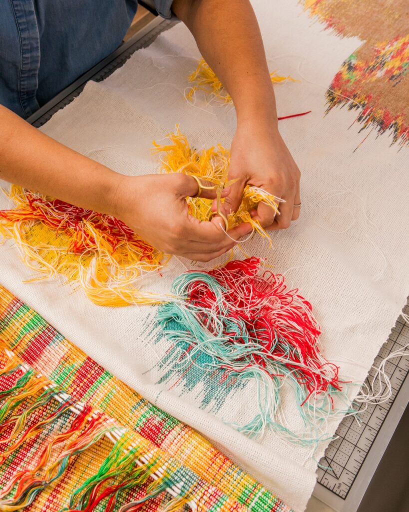 An artist trims yellow fibers for textile arts.